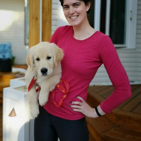 Portrait of Niamh Mulcahy in a red top and cradling a puppy under her arm.