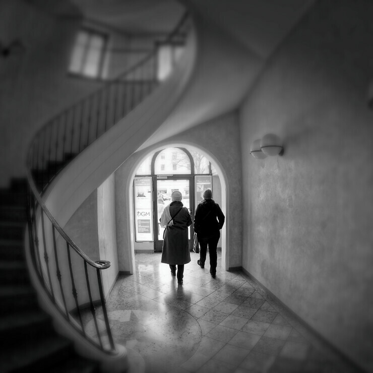 Photograph of two women are walking towards the exit doors of an old fashioned apartment building.