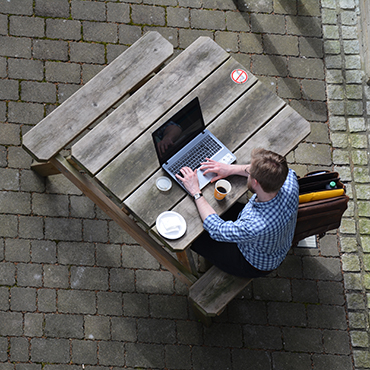 Person sitting at a picnic table and working on a laptop, seen from above.