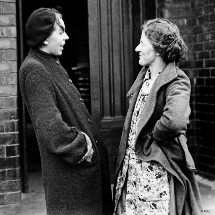 Black and white photograph of two women talking in the street in the mid 1900s.