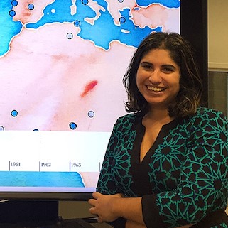 Roopika Risam in front of a screens showing a world map.