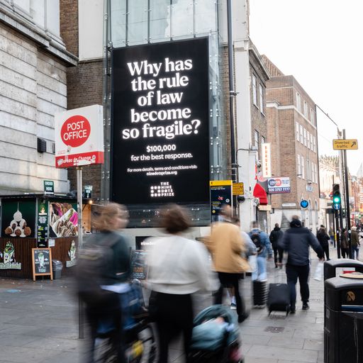 A busy street scene in London with people waling was a billboard that reads 'Why has the rule of law become so fragile?'