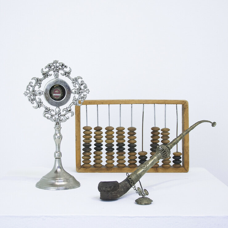 An abacus, antique pipe and ornate thermometer on a plinth.