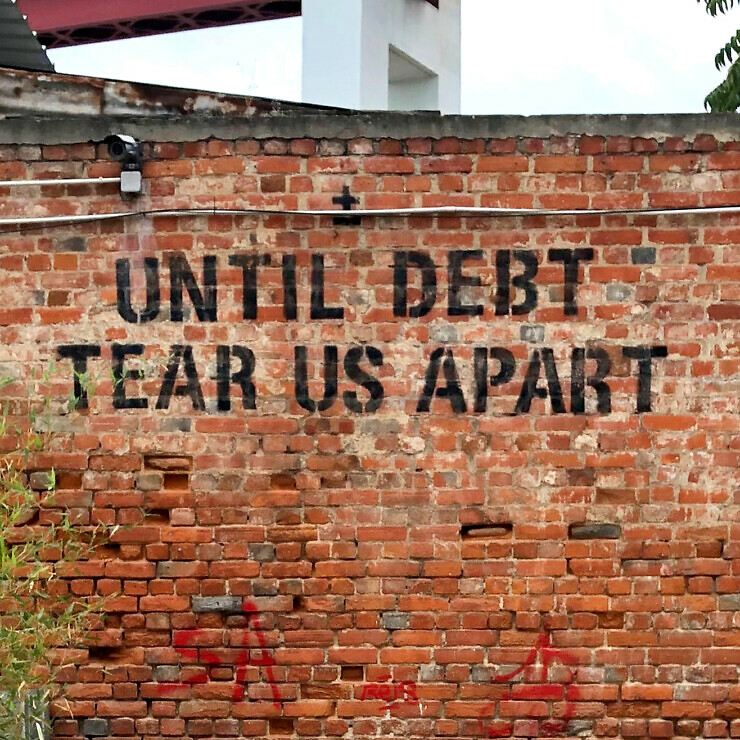 A brick wall has the words 'Until Debt Tear Us Apart' graffitied on it.