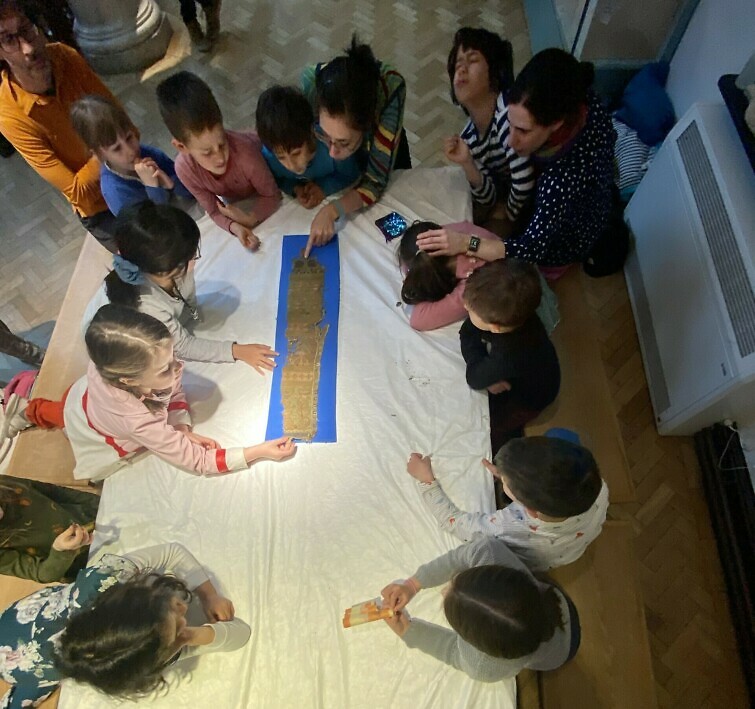 Children crowding round a table looking at a manuscript