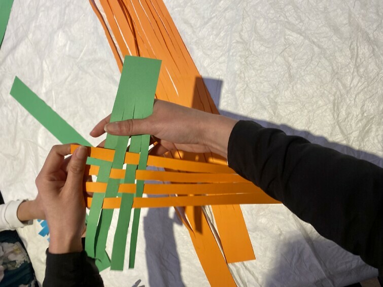 Hands weaving green and orange paper together