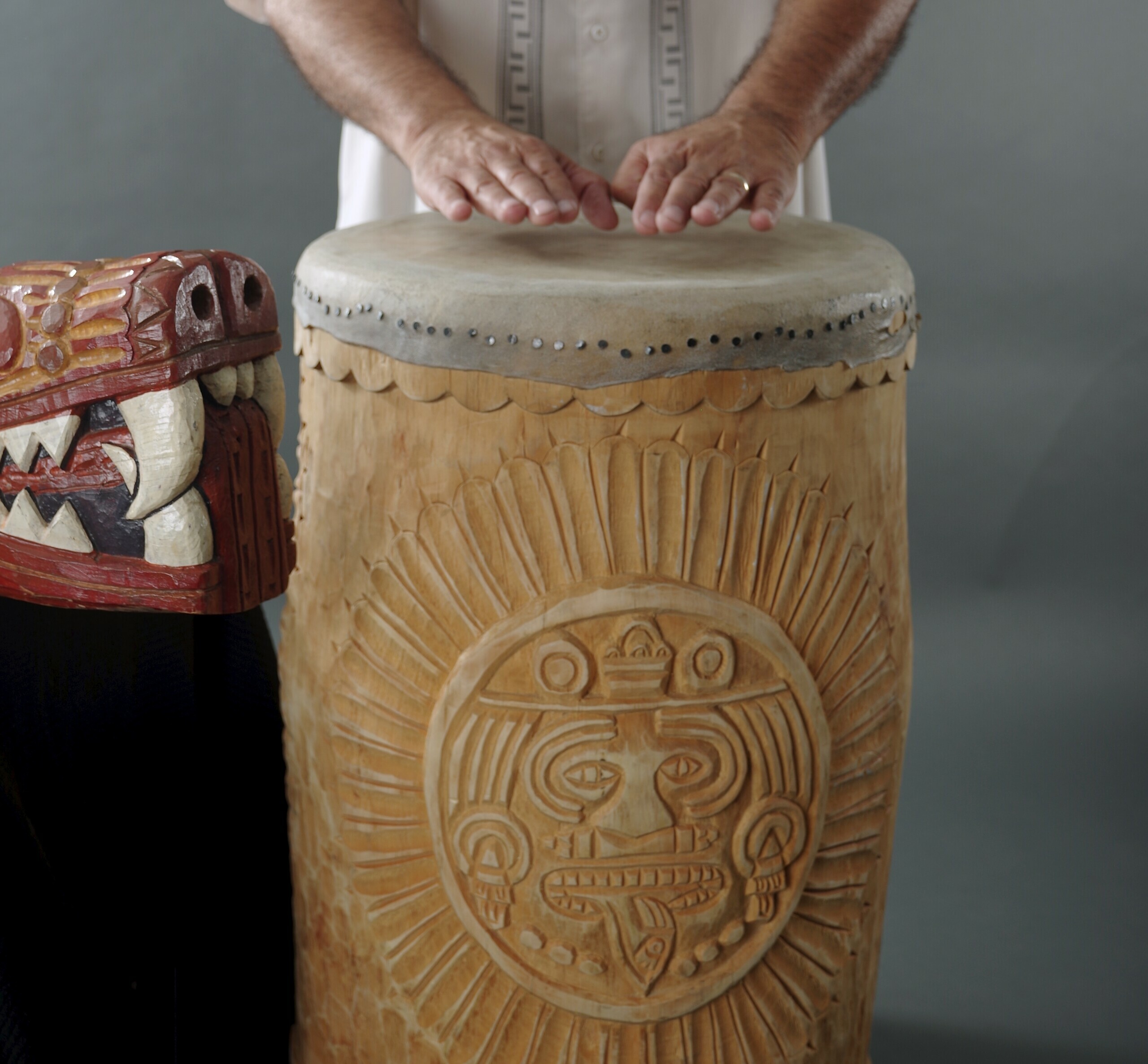 hands beating a tall wooden carved drum