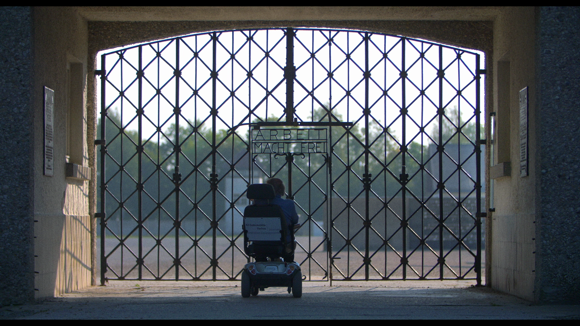 Person in a wheelchair in front of concentration camp gates