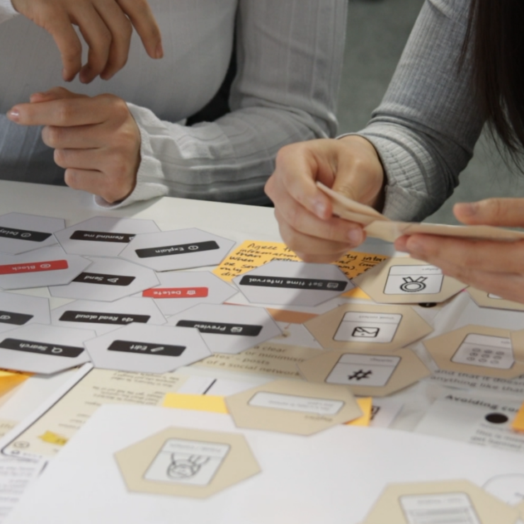 Two workshop participants sitting side by side and looking through design cards laid out on a desk in front of them