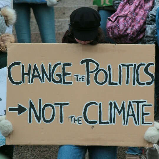 Person holding a placard that says change politics not climate