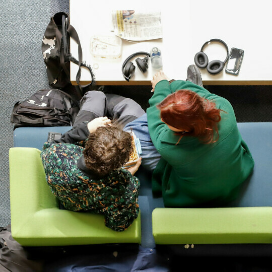 Two people are sitting at a low coffee table in the atrium of the Alison Richard Building, seen from above.